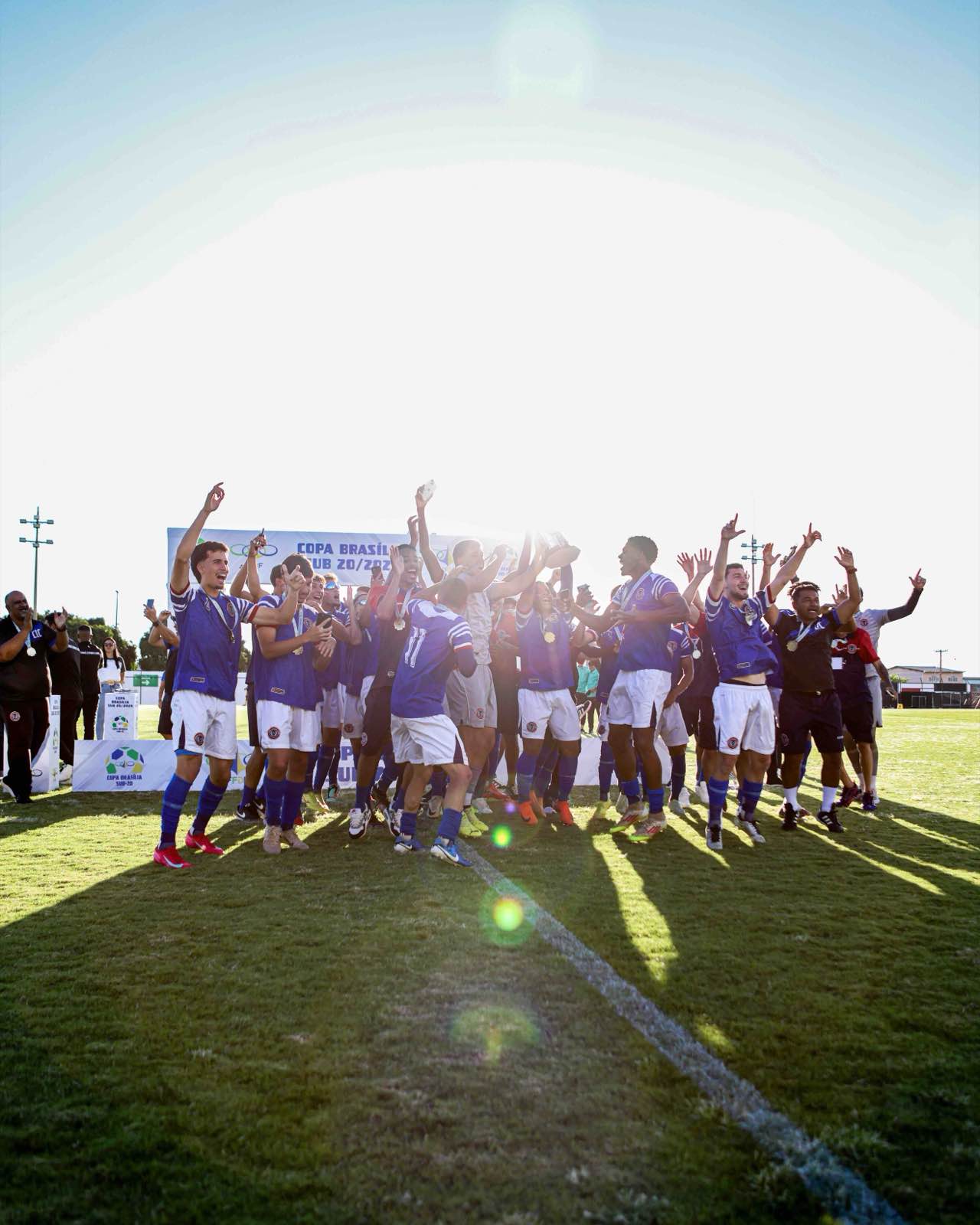 Jogadores do Canaã erguem a taça da Copa Brasília em contraluz, no fim da tarde.